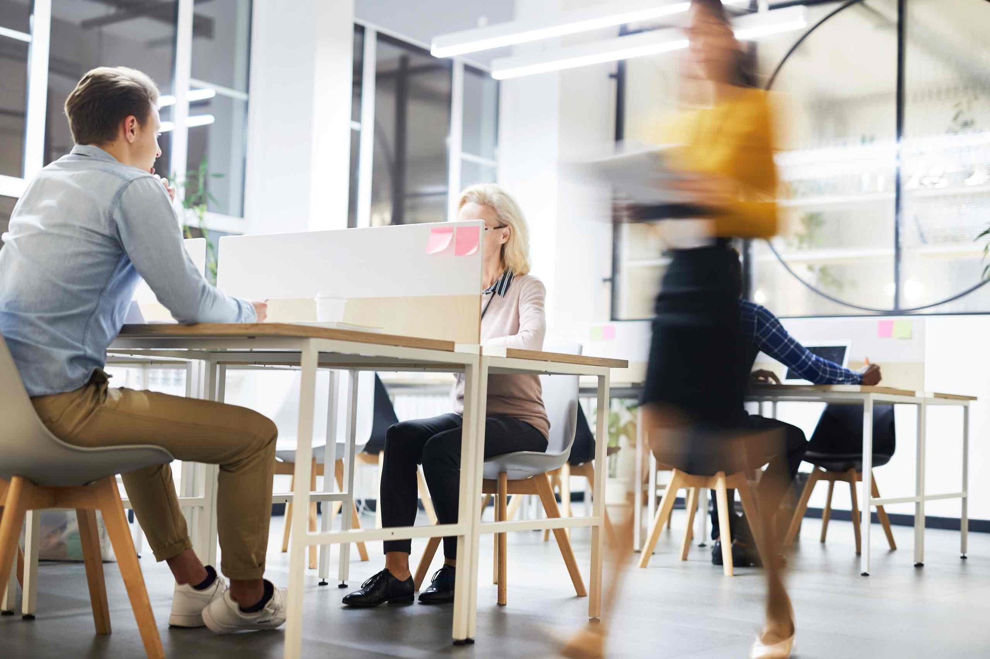 A busy open-plan office with some workers sitting and others walking.