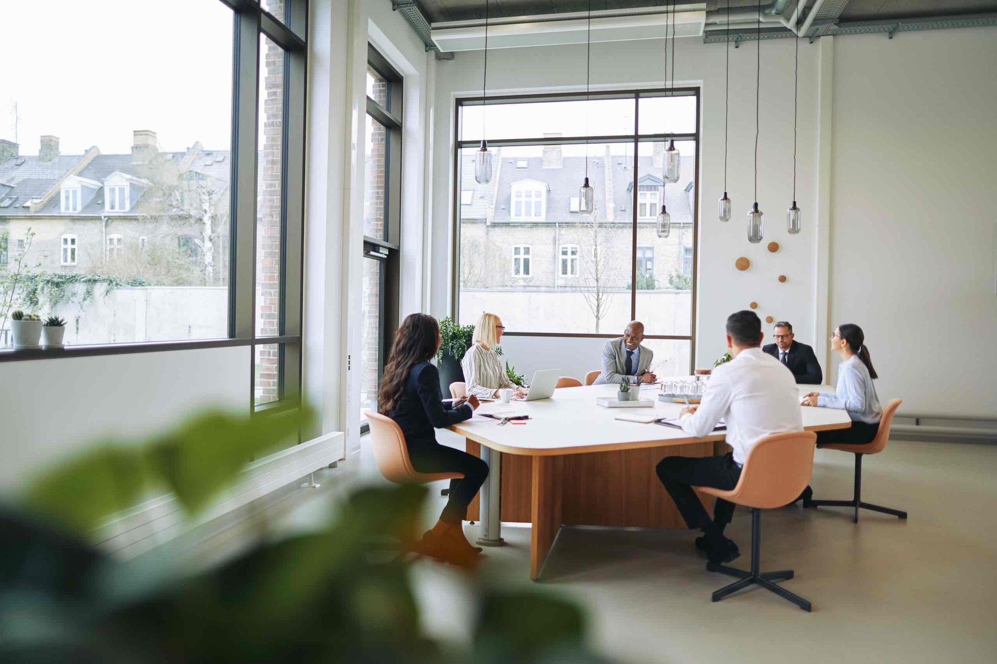 Six business people sitting around a board table in a light-filled office.