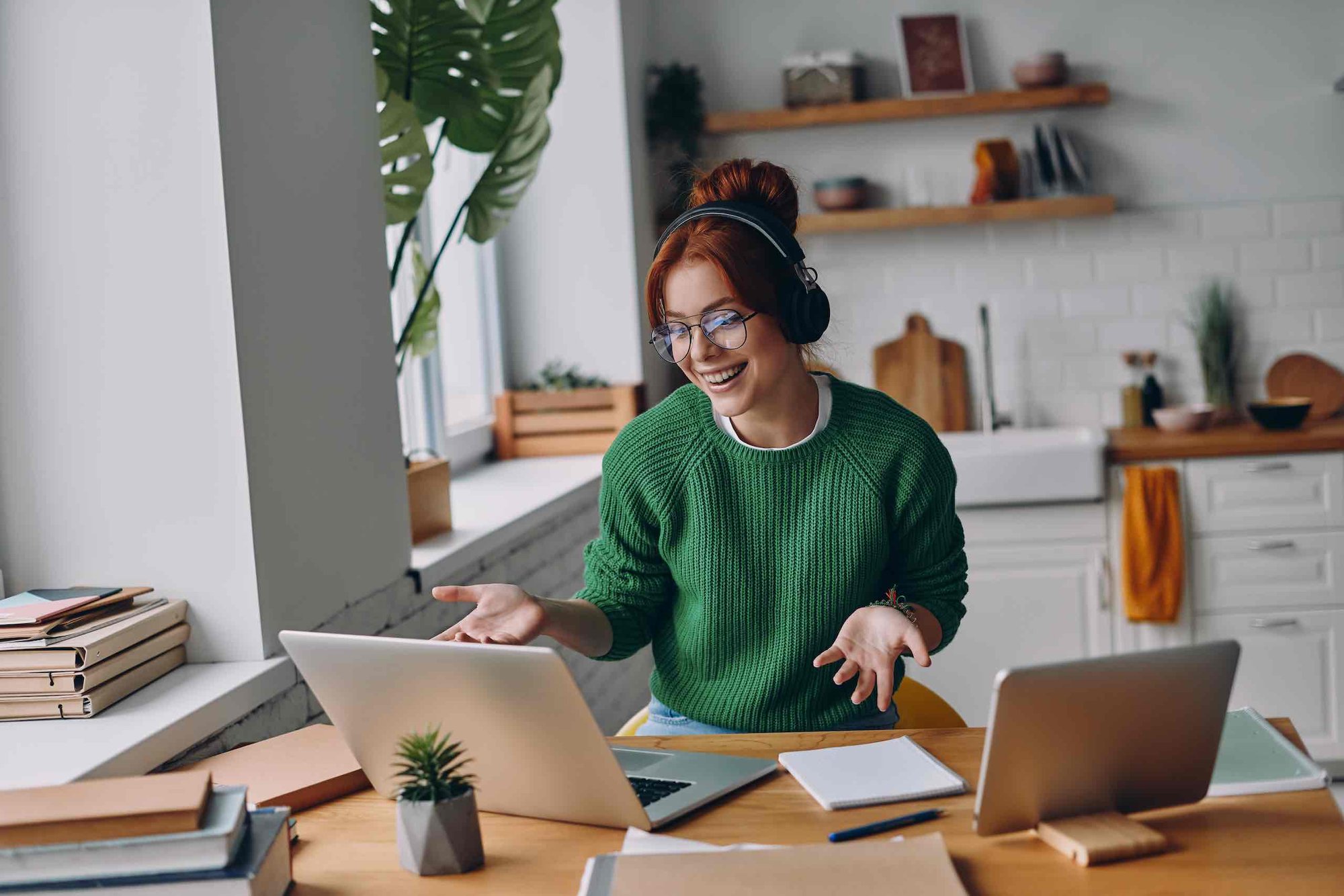 A cheerful woman is on a video call. She has two laptops and is working from home.