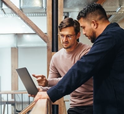 Two men standing at a rail with laptop