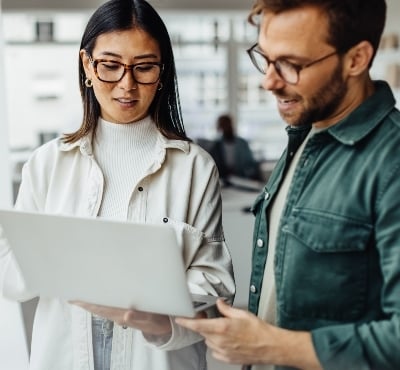 Man and woman standing, looking at laptop.