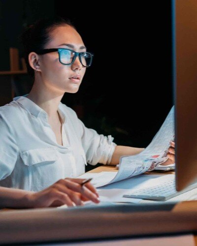 A woman compares paper documents with data on a computer screen.