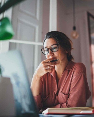 A pensive woman sitting at a desk at a computer screen.