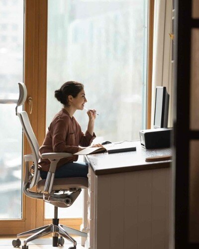 Side view of a happy woman sitting in an ergonomic office chair at her computer.