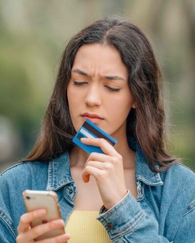 A woman looks at her phone while holding a credit card. Phishing scams can entice people to provide personally identifiable information.