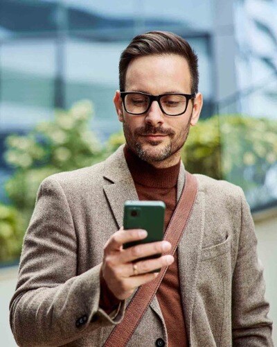 A businessman in a light brown jacket looks at his phone.