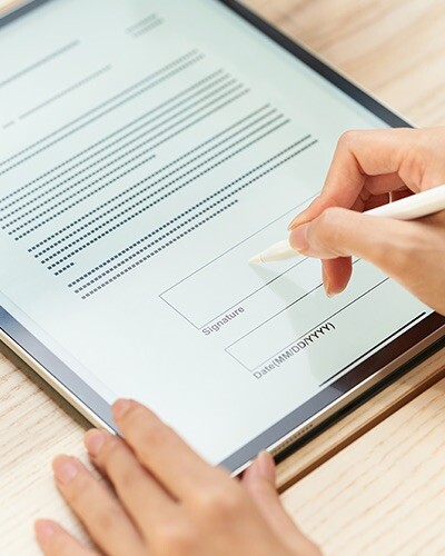 Close up of hands holding a stylus in preparation to sign a digital document on a tablet.