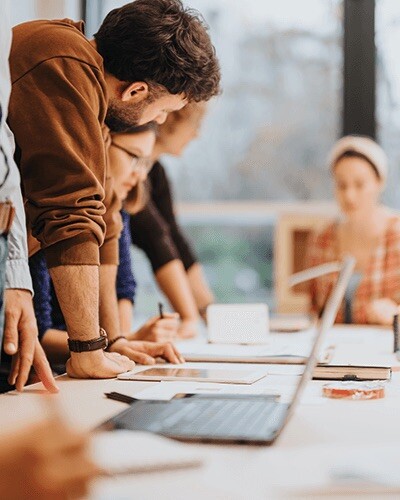 Two workers lean against a desk and look intently at a screen. Choosing sustainable partners is important in the modern business environment.