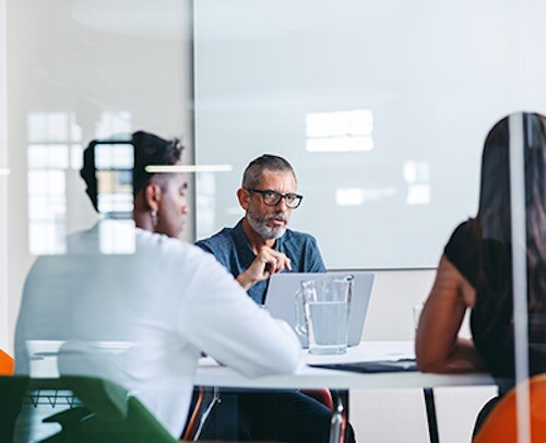 Employees sit in a conference room at a desk. To keep up with the changing digital landscape, companies need to transform quickly.